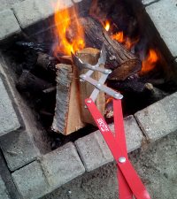 A person uses the BBQ Croc 26-inch barbecue tongs for grilling to move logs in a burning fire pit safely. 